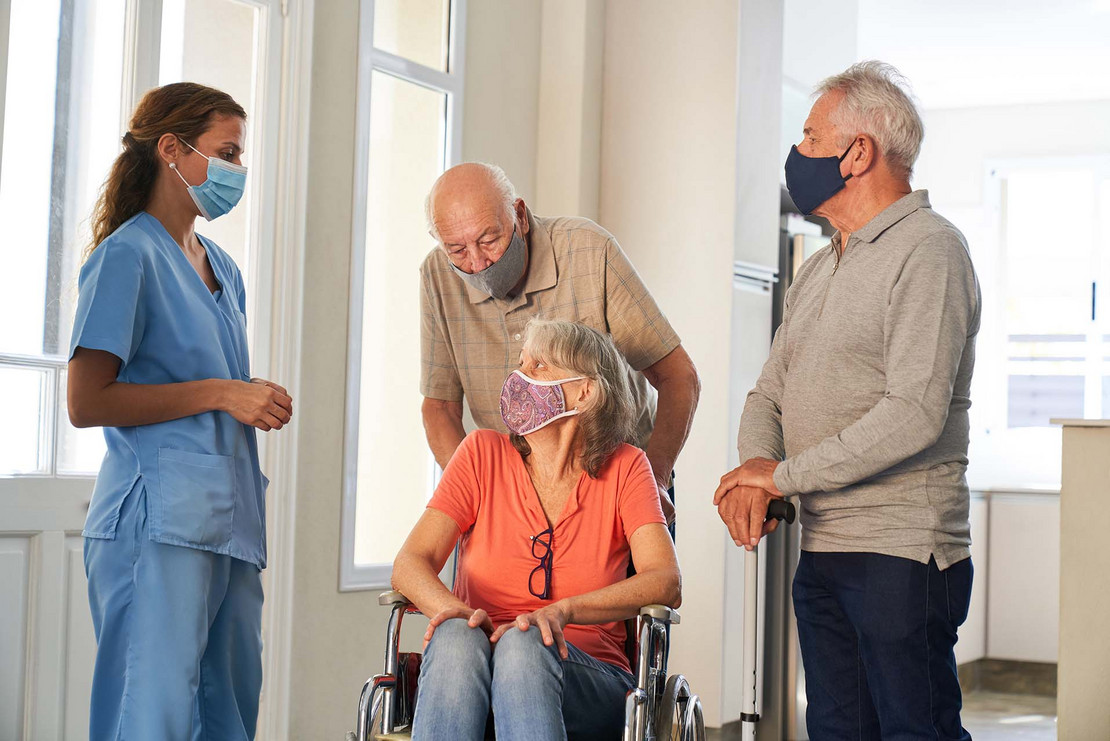 Mann schiebt seine Frau im Rollstuhl, eine Krankenschwester steht daneben. 