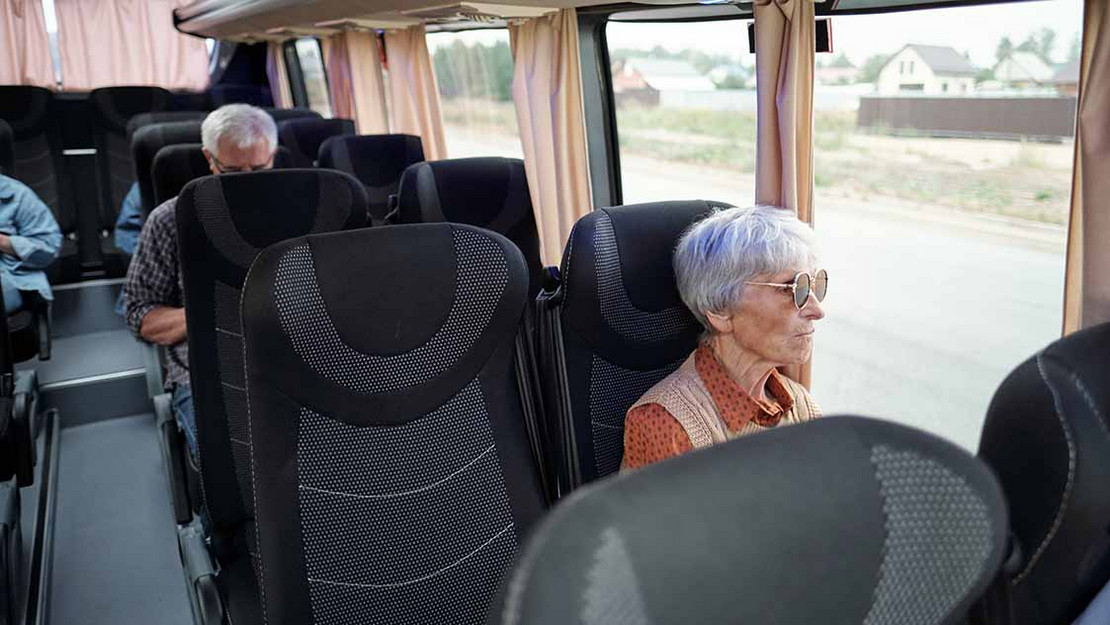 Ältere Frau sitzt in einem Reisebus und blickt aus dem Fenster. 